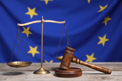 Scales of justice and judge's gavel on wooden table against European Union flag