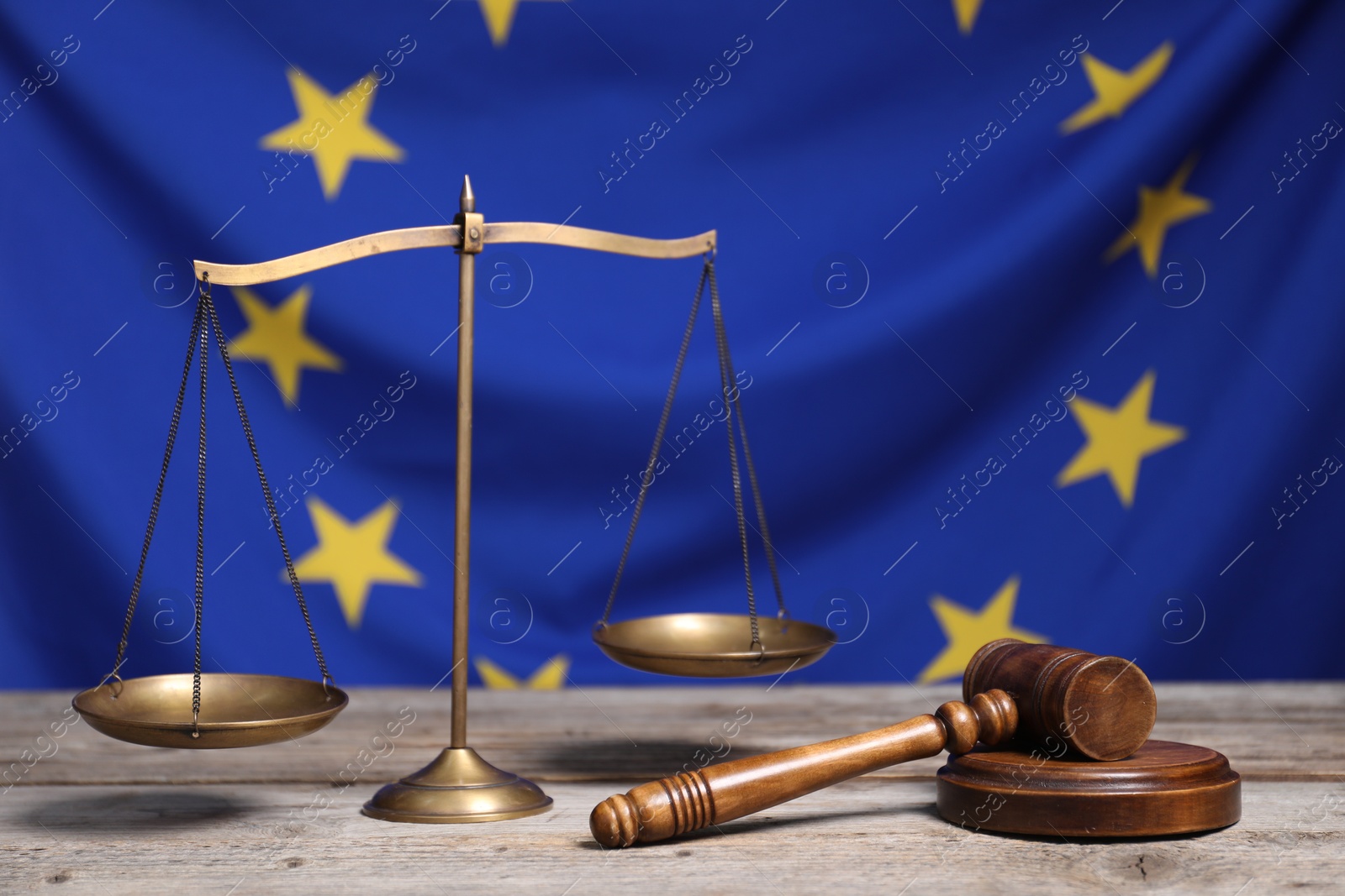 Photo of Scales of justice and judge's gavel on wooden table against European Union flag