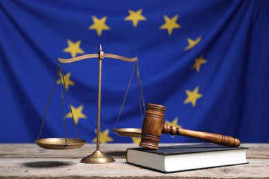 Scales of justice, judge's gavel and book on wooden table against European Union flag