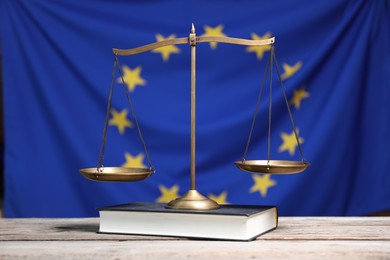 Photo of Scales of justice and book on wooden table against European Union flag