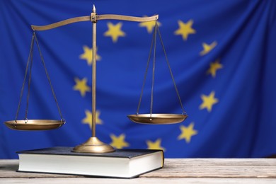 Scales of justice and book on wooden table against European Union flag, space for text