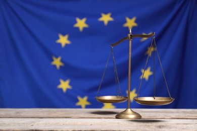 Scales of justice on wooden table against European Union flag, space for text