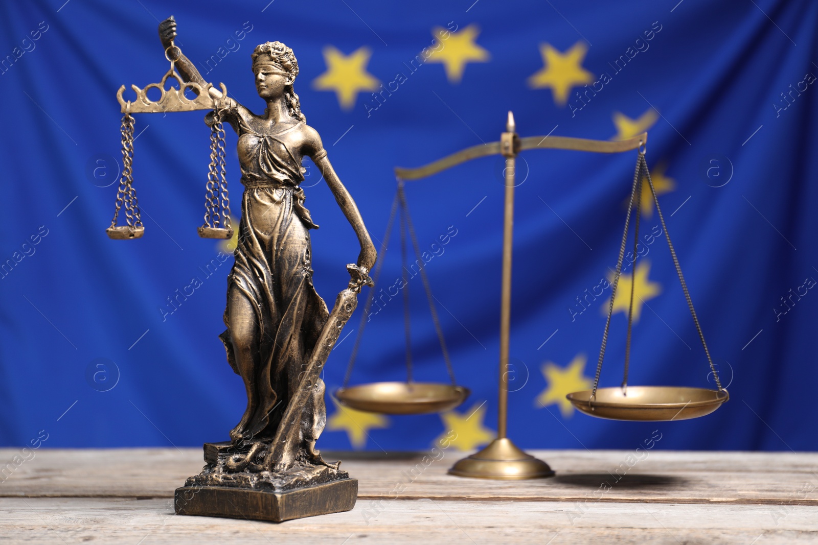 Photo of Figure of Lady Justice and scales on wooden table against European Union flag