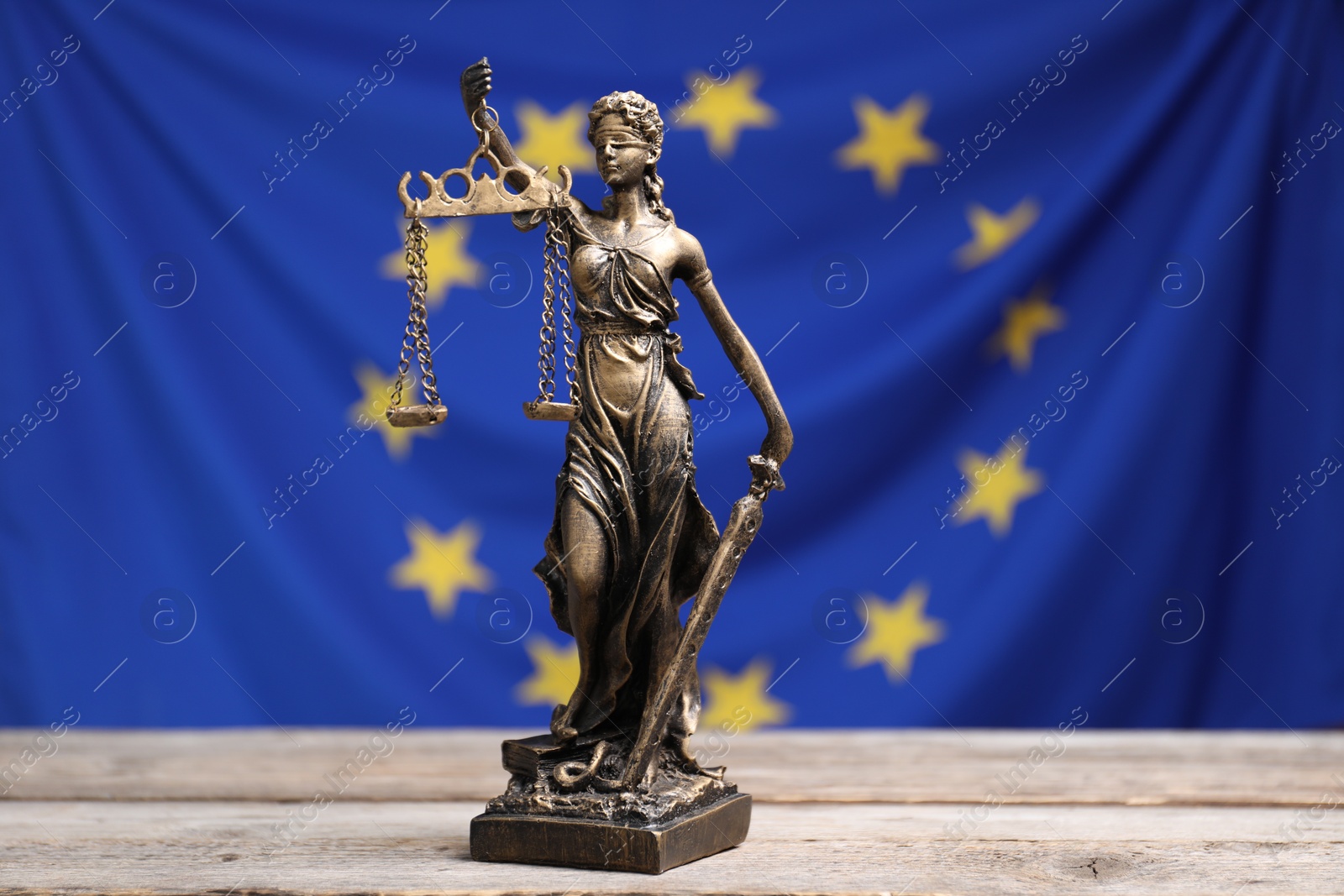 Photo of Figure of Lady Justice on wooden table against European Union flag