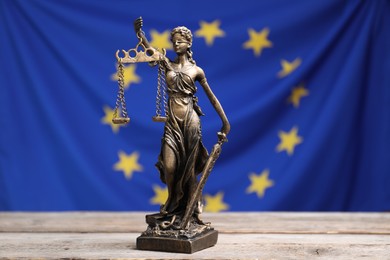 Photo of Figure of Lady Justice on wooden table against European Union flag