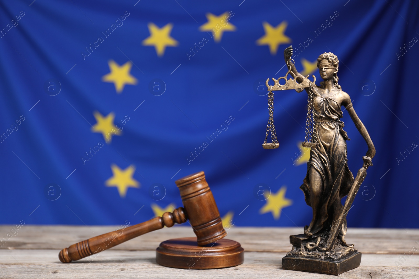 Photo of Figure of Lady Justice and judge's gavel on wooden table against European Union flag