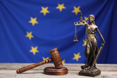 Photo of Figure of Lady Justice and judge's gavel on wooden table against European Union flag