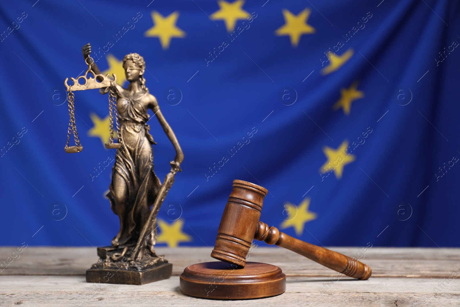 Photo of Figure of Lady Justice and judge's gavel on wooden table against European Union flag