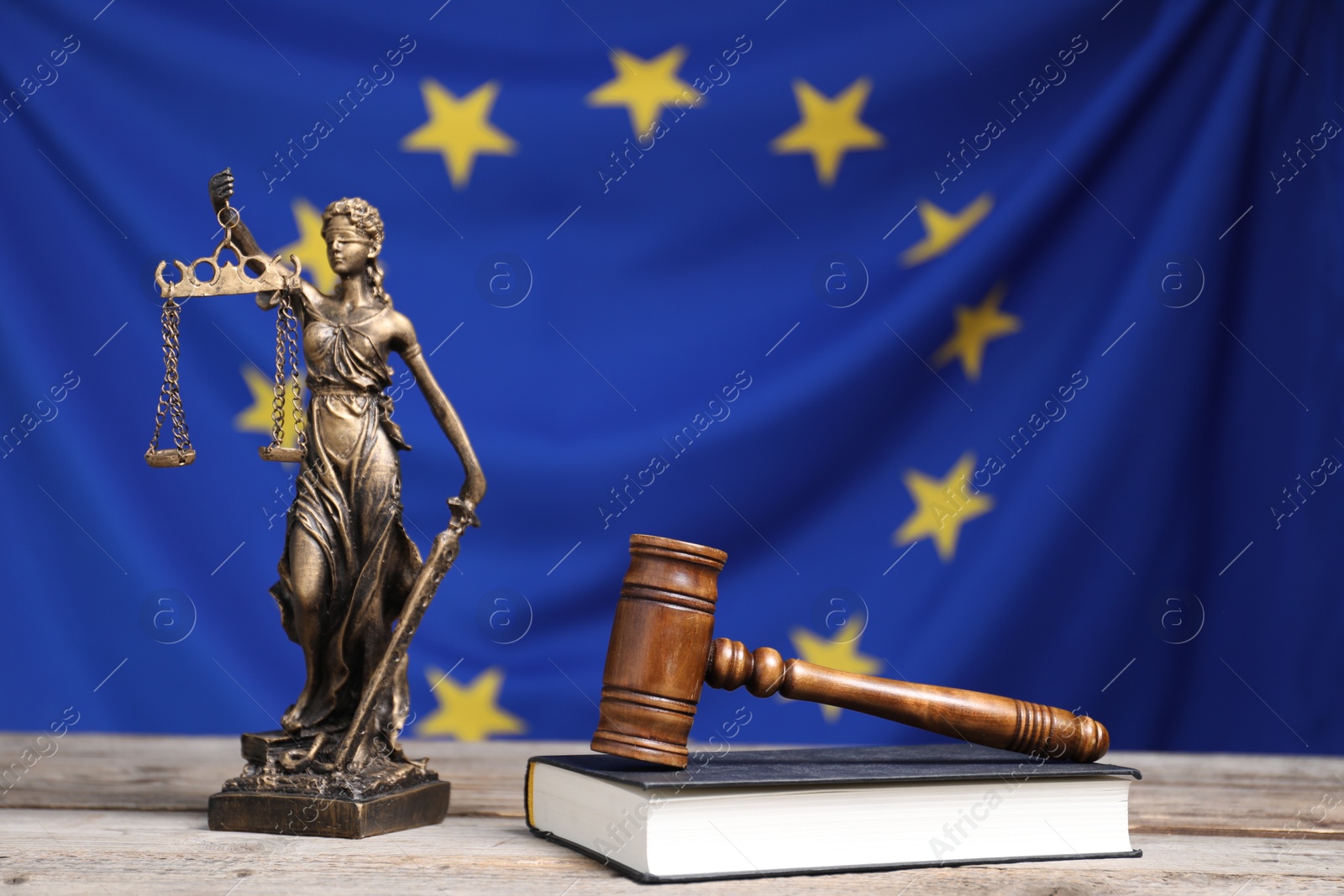 Photo of Figure of Lady Justice, judge's gavel and book on wooden table against European Union flag