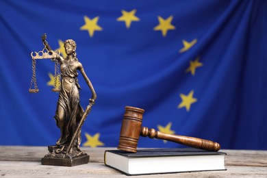 Figure of Lady Justice, judge's gavel and book on wooden table against European Union flag