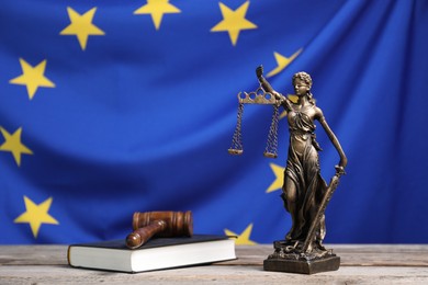 Figure of Lady Justice, judge's gavel and book on wooden table against European Union flag