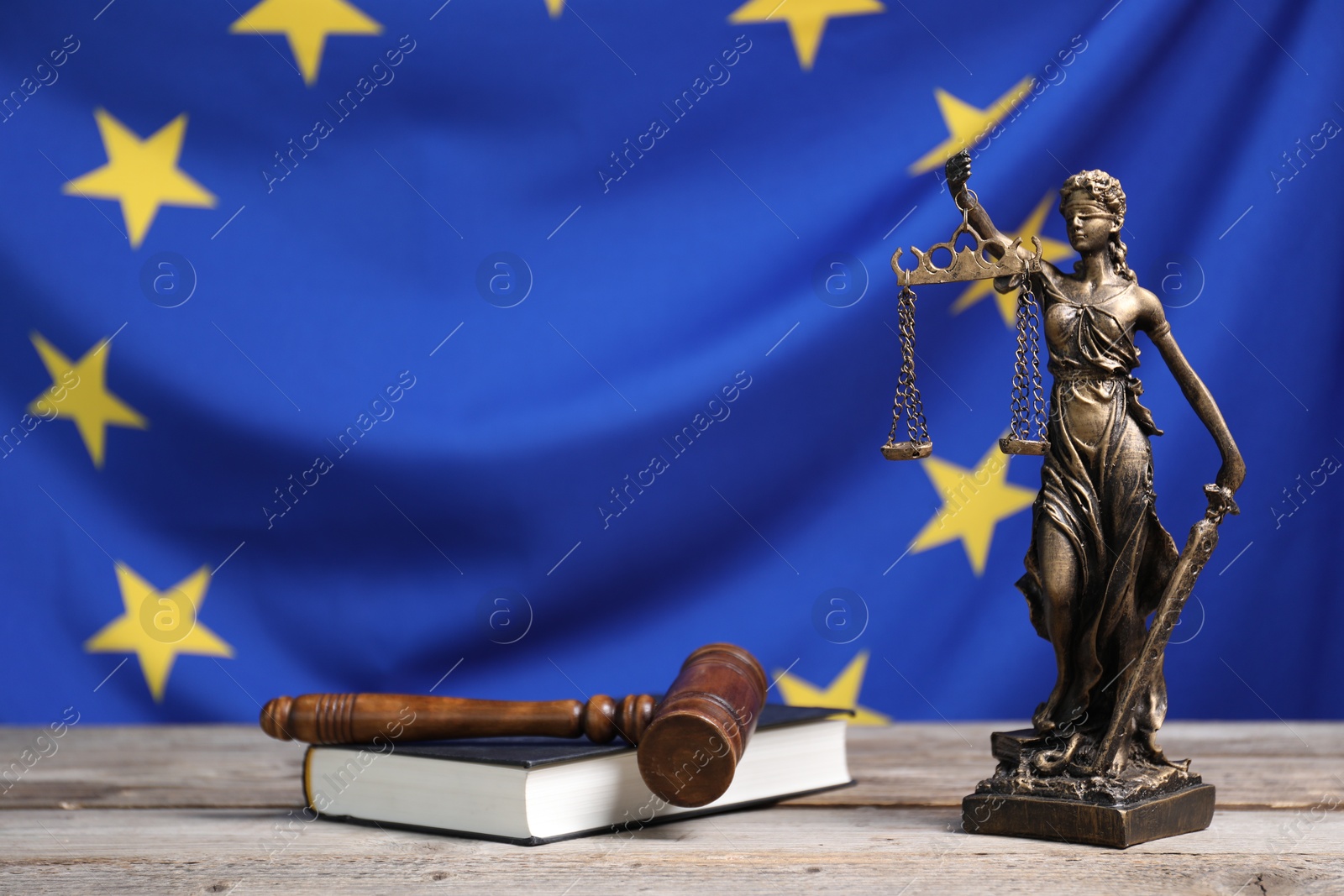 Photo of Figure of Lady Justice, judge's gavel and book on wooden table against European Union flag