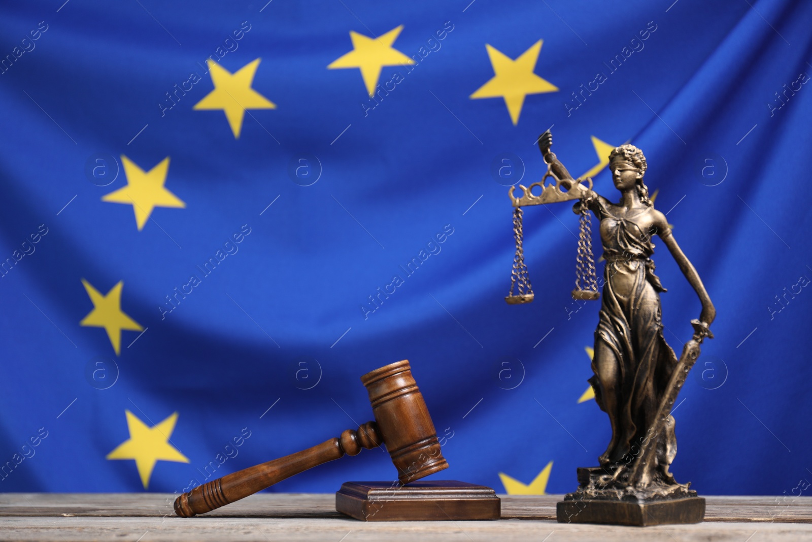 Photo of Figure of Lady Justice, judge's gavel and book on wooden table against European Union flag