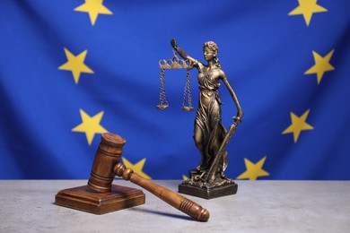 Photo of Figure of Lady Justice and judge's gavel on table against European Union flag