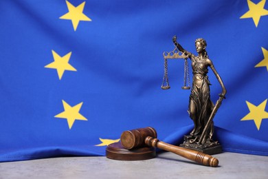 Photo of Figure of Lady Justice and judge's gavel on table against European Union flag