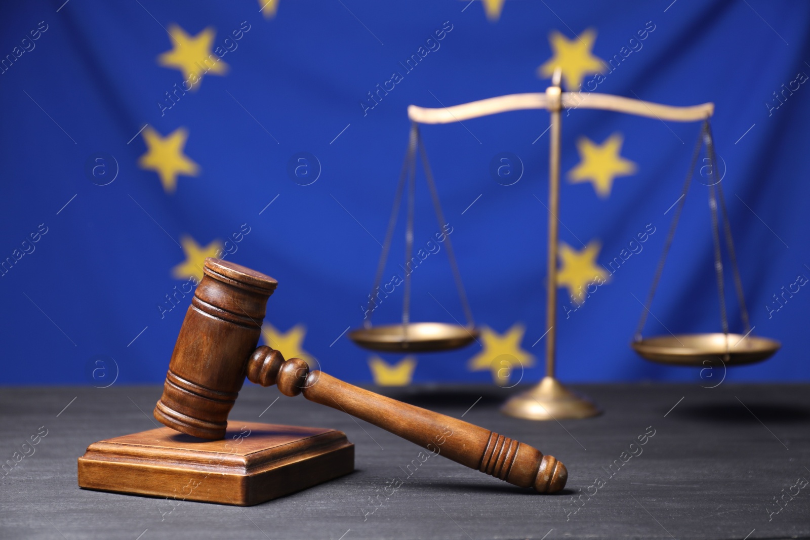 Photo of Judge's gavel and scales of justice on grey table against European Union flag