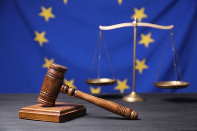 Photo of Judge's gavel and scales of justice on grey table against European Union flag