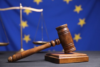 Judge's gavel and scales of justice on grey table against European Union flag, closeup