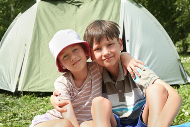 Photo of Girl and her brother spending time together near camping tent outdoors