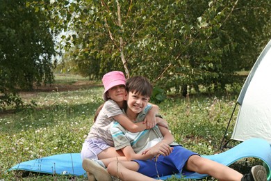 Photo of Girl and her brother spending time together near camping tent outdoors