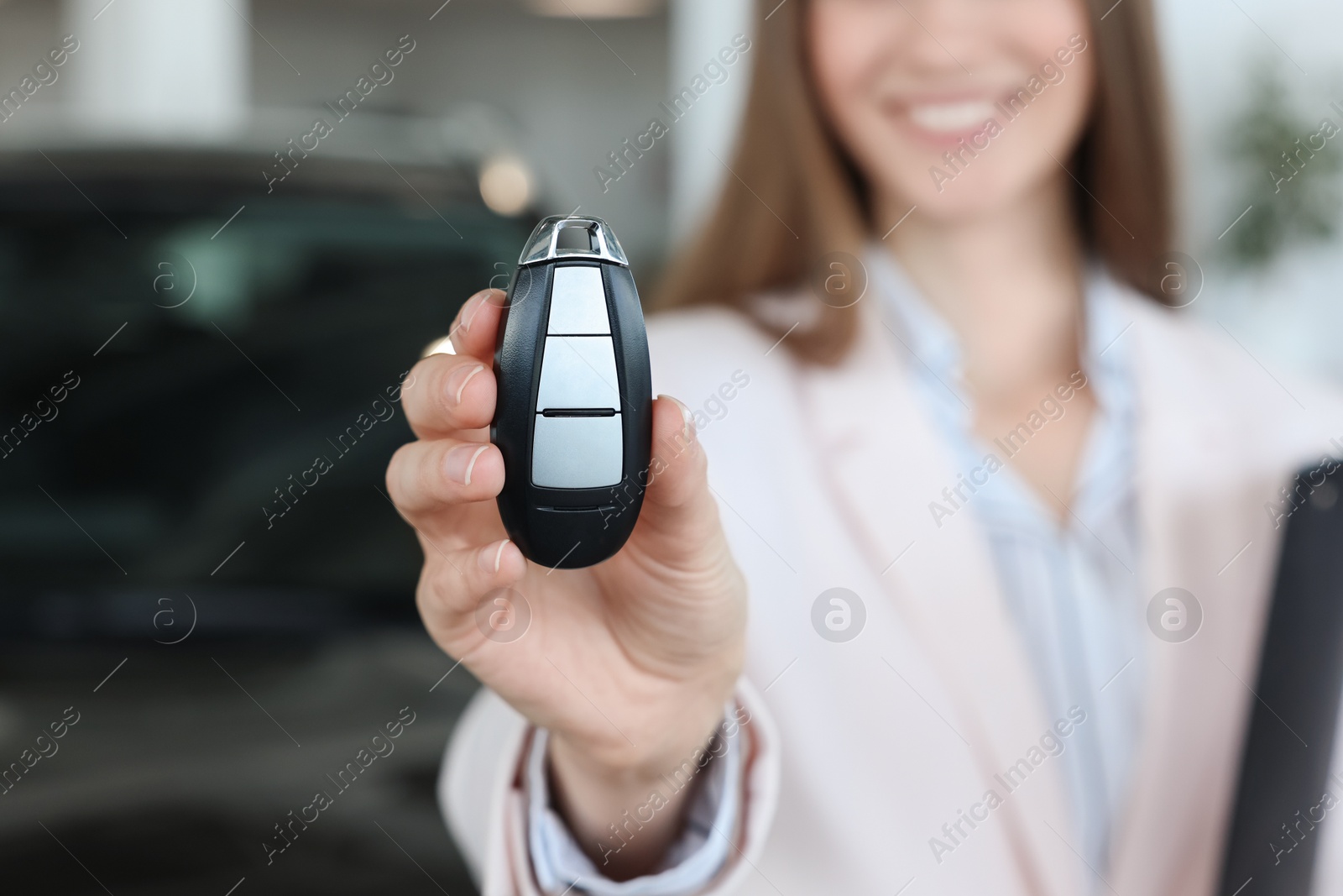 Photo of Happy saleswoman holding key near new black car in salon, closeup