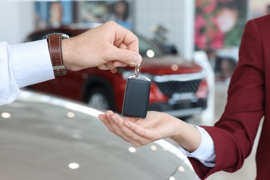 Photo of Salesman giving key to client near new car in salon, closeup