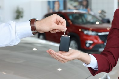 Salesman giving key to client near new car in salon, closeup