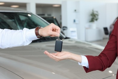 Photo of Salesman giving key to client near new car in salon, closeup