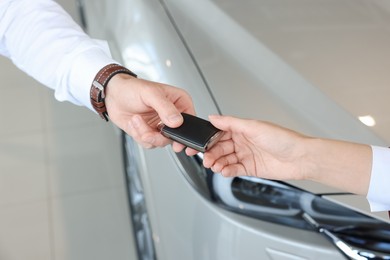 Photo of Salesman giving key to client near new car in salon, closeup