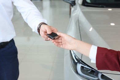 Salesman giving key to client near new car in salon, closeup