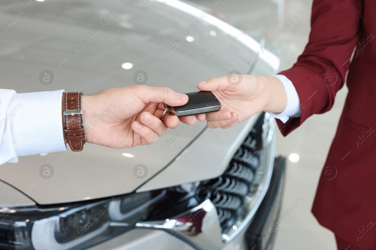 Photo of Salesman giving key to client near new car in salon, closeup