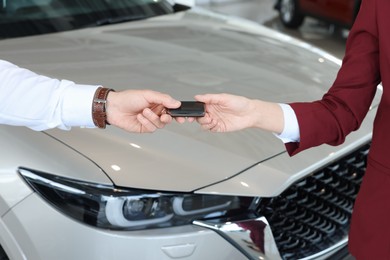 Photo of Salesman giving key to client near new car in salon, closeup