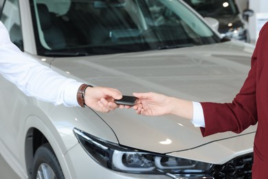 Photo of Salesman giving key to client near new car in salon, closeup