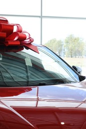 Photo of Luxury vehicle. New modern red car with bow in salon, closeup