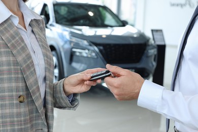 Photo of Saleswoman giving key to client near new car in salon, closeup