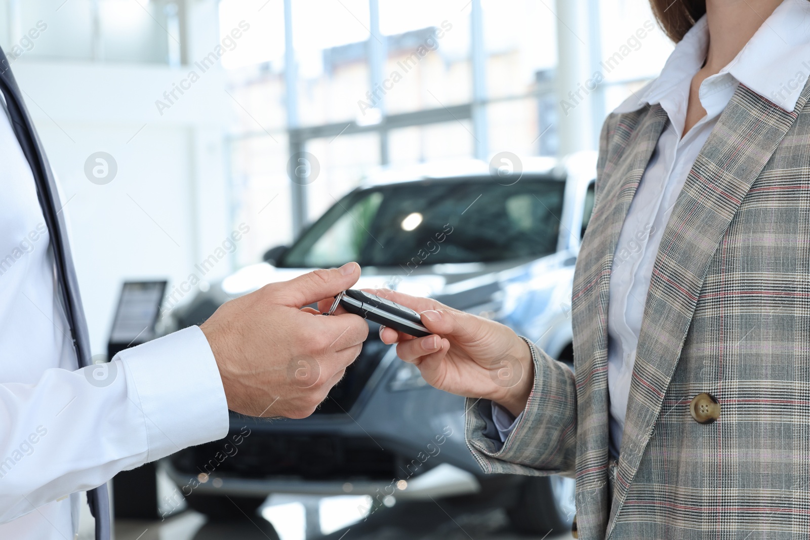 Photo of Saleswoman giving key to client near new car in salon, closeup