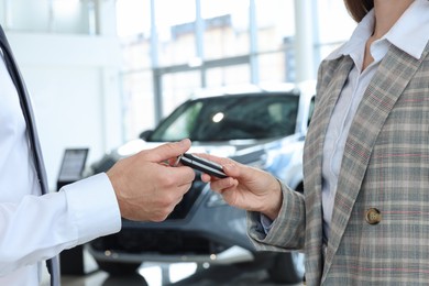 Photo of Saleswoman giving key to client near new car in salon, closeup