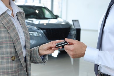 Photo of Saleswoman giving key to client near new car in salon, closeup