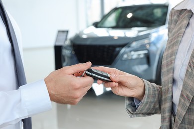 Photo of Saleswoman giving key to client near new car in salon, closeup