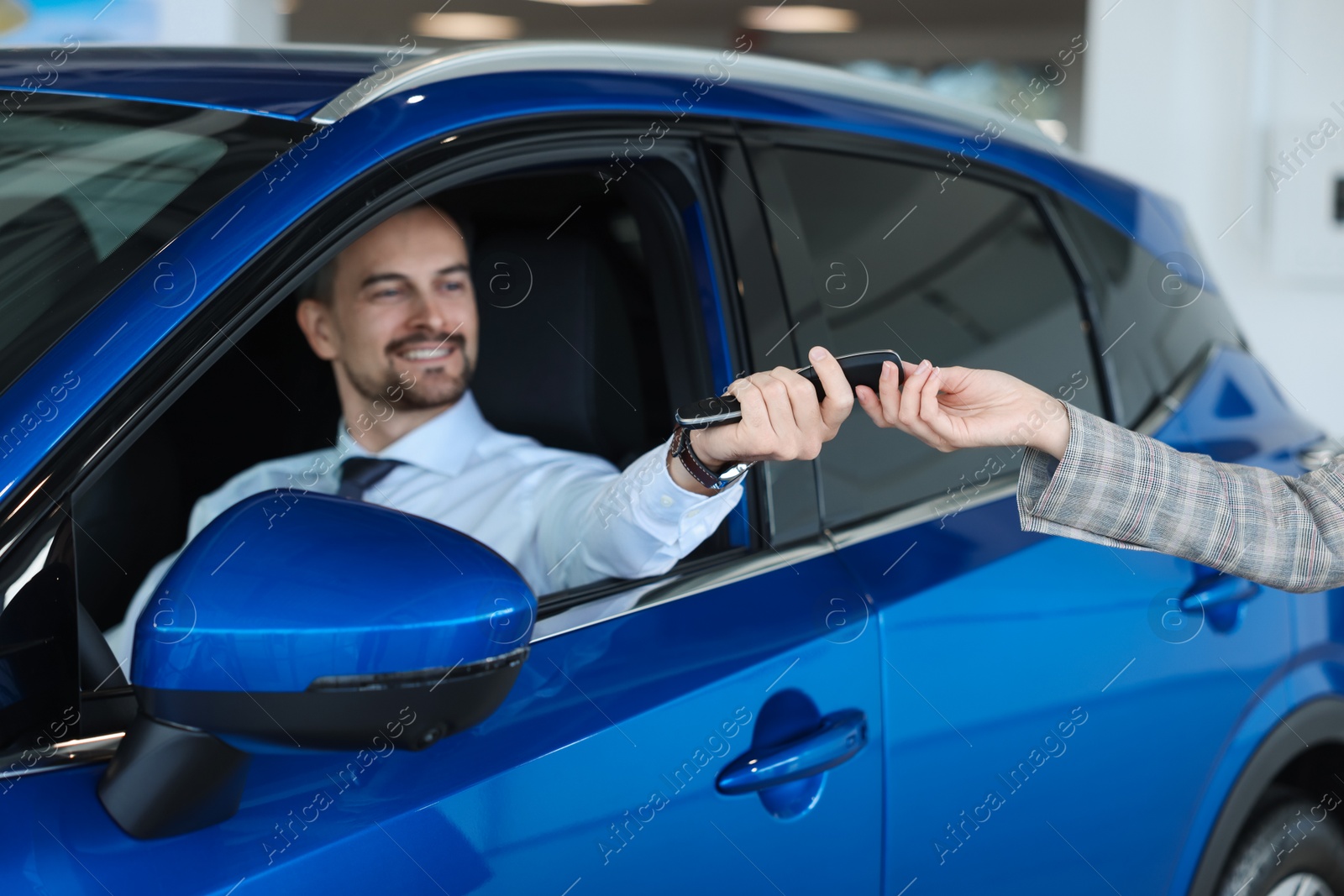 Photo of Saleswoman giving key to client inside new car in salon, selective focus