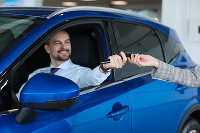 Saleswoman giving key to client inside new car in salon, selective focus