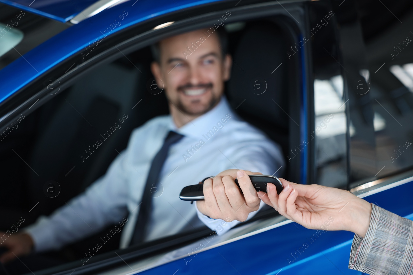 Photo of Saleswoman giving key to client inside new car in salon, selective focus