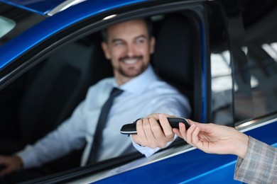 Photo of Saleswoman giving key to client inside new car in salon, selective focus