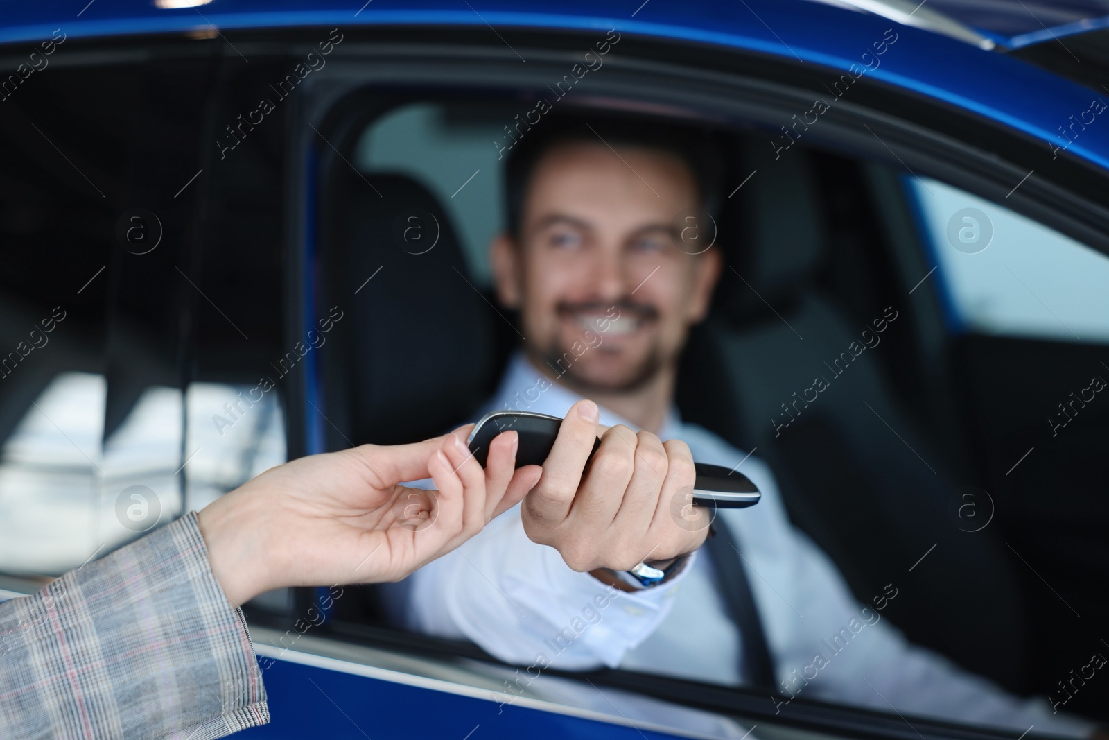 Photo of Saleswoman giving key to client inside new car in salon, selective focus