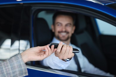 Saleswoman giving key to client inside new car in salon, selective focus