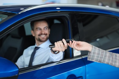 Saleswoman giving key to client inside new car in salon, selective focus