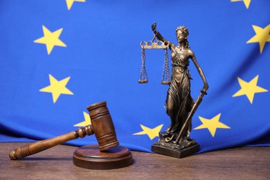 Judge's gavel, figure of Lady Justice and European Union flag on wooden table