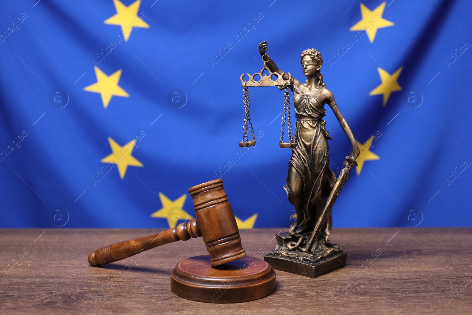 Photo of Figure of Lady Justice and judge's gavel on wooden table against European Union flag