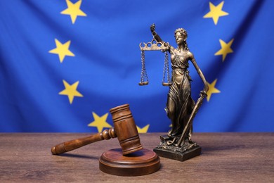 Photo of Figure of Lady Justice and judge's gavel on wooden table against European Union flag