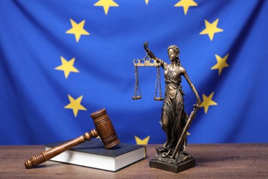 Figure of Lady Justice, judge's gavel and book on wooden table against European Union flag